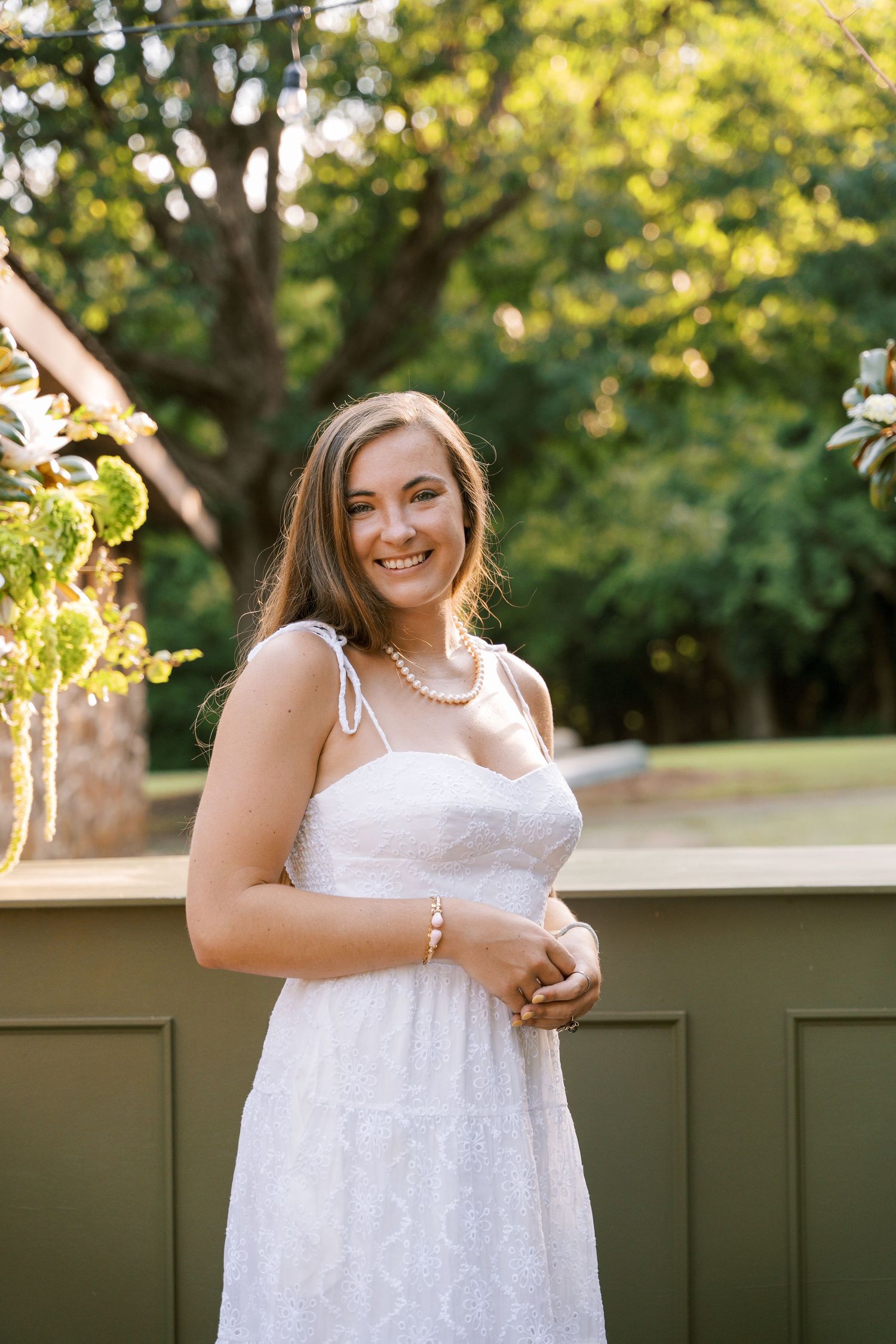 Woman in white summer dress with pearl necklace standing outdoors.