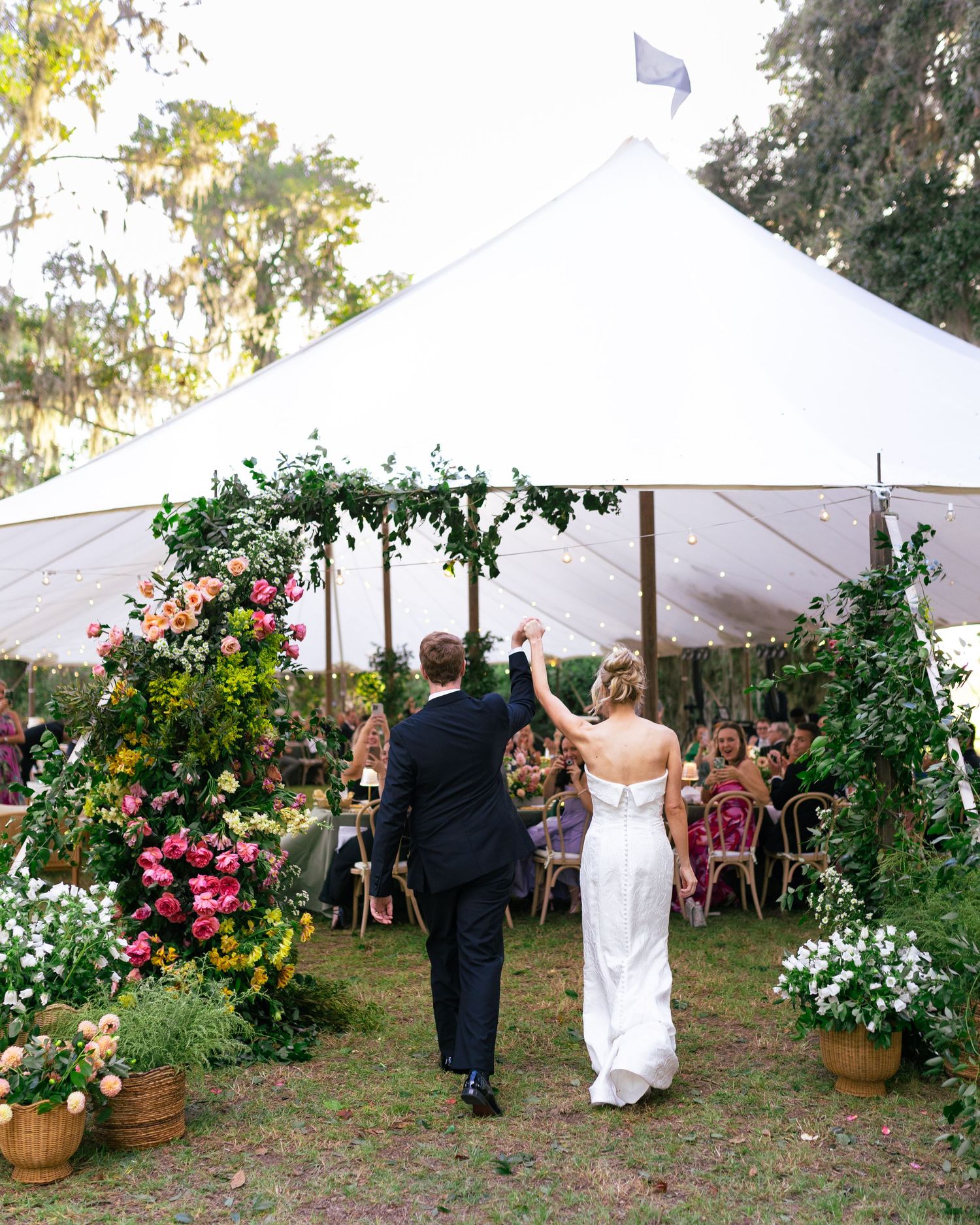 Couple entering white wedding tent decorated with floral arches and greenery.