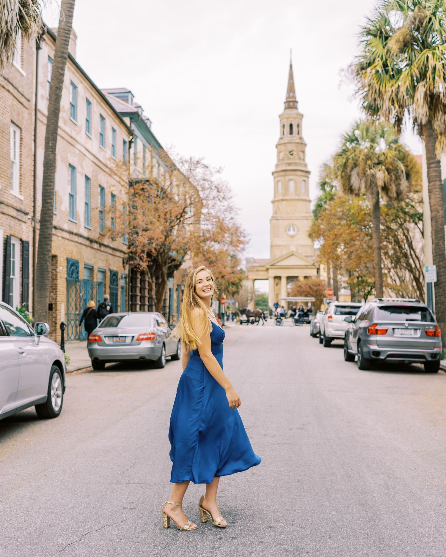 A blue dress flows elegantly against historic Charleston architecture and palm trees.