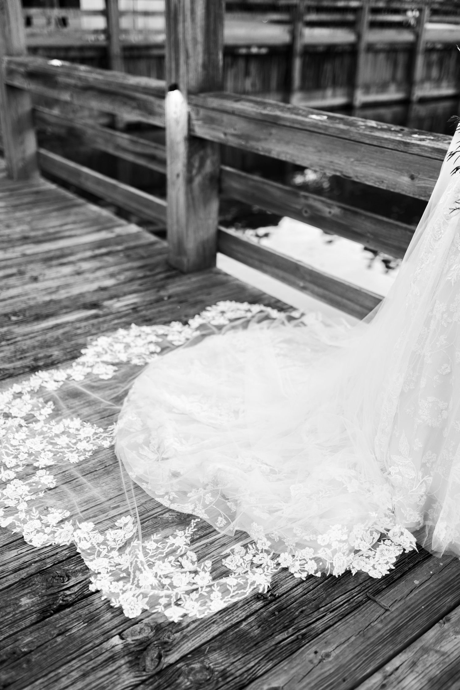 Lace wedding dress train spreads across weathered wooden dock boards.