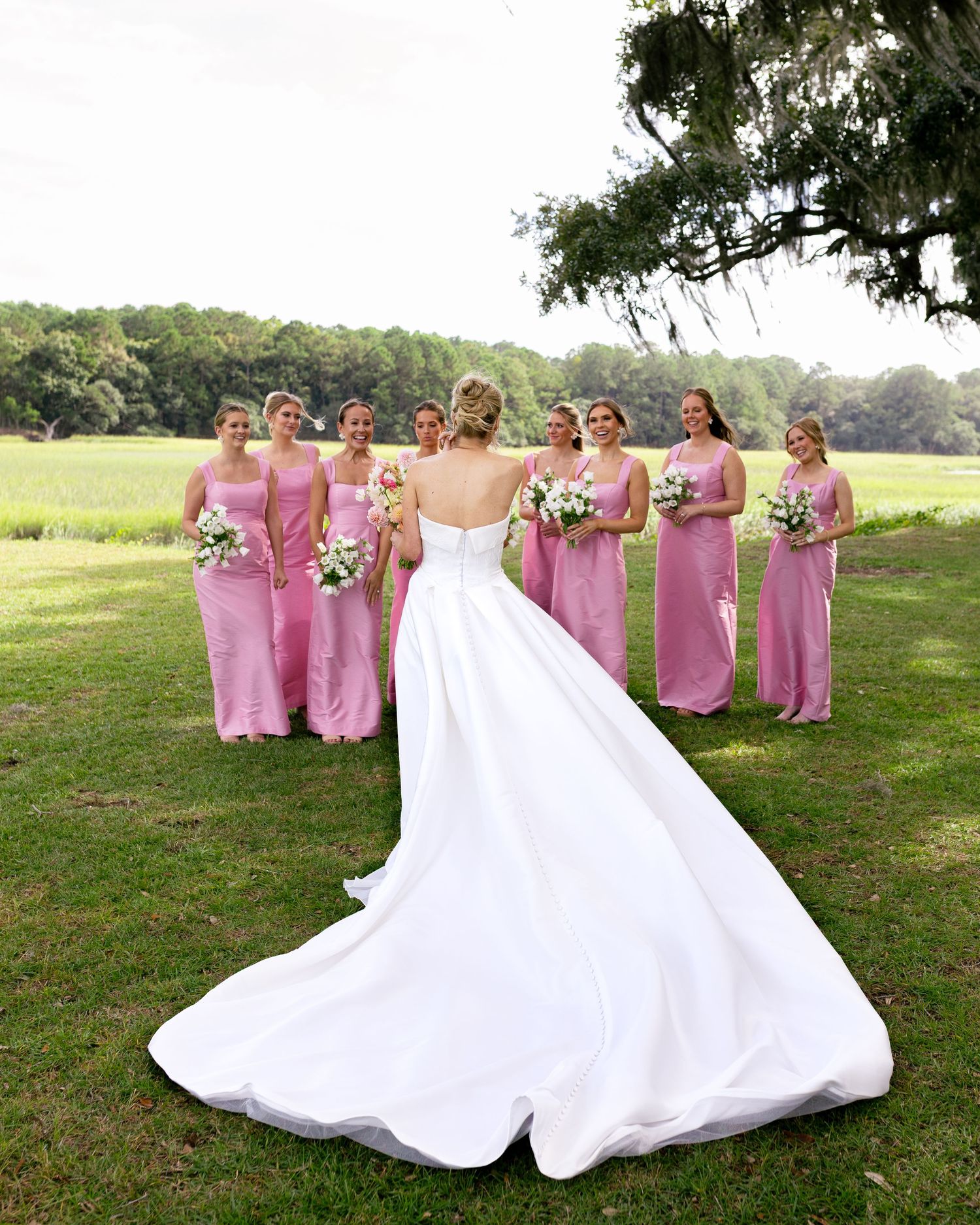 Wedding party in pink bridesmaid dresses posing on a grassy hillside with a white-gowned bride.