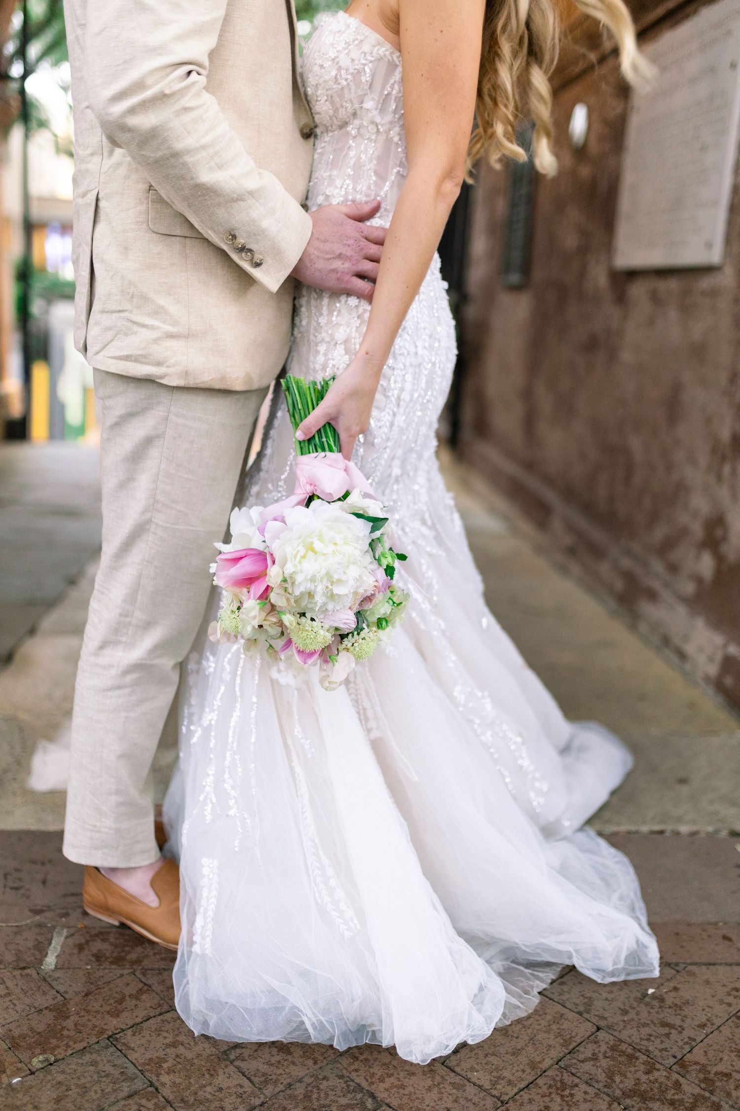 Wedding couple embracing, showing details of white lace dress and light beige suit.
