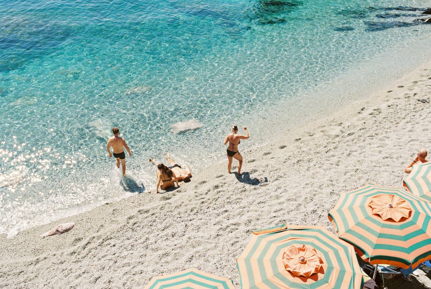 Beach scene with colorful striped umbrellas and crystal clear turquoise Mediterranean waters.