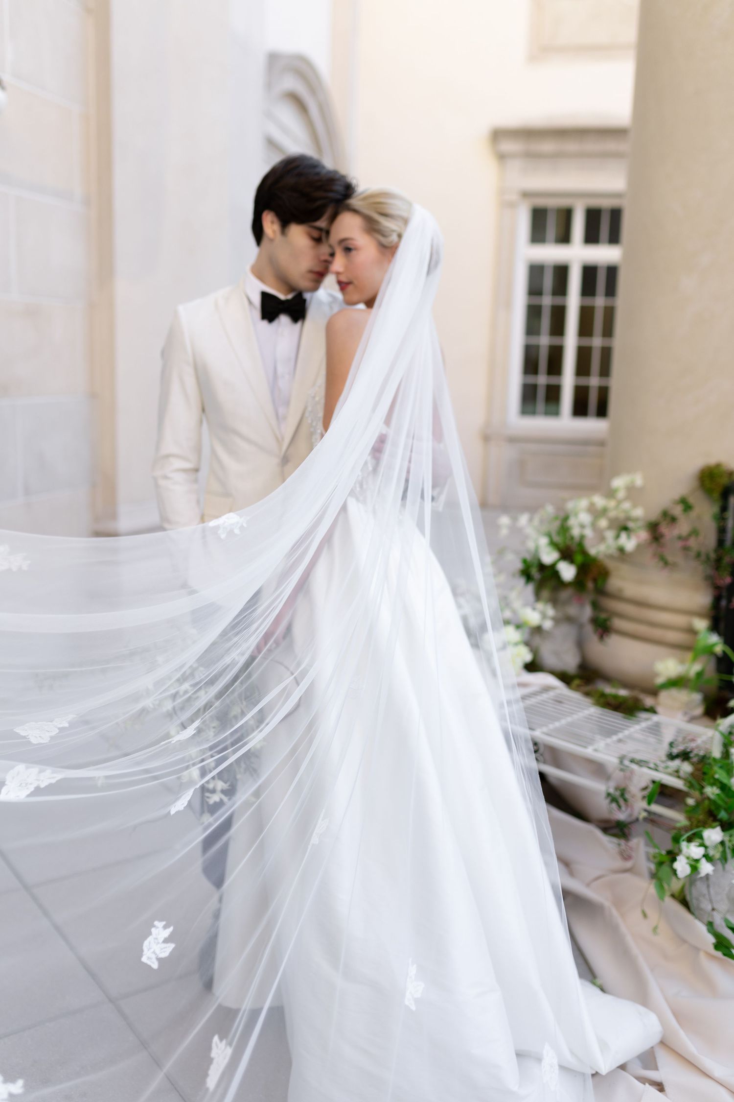 Romantic wedding portrait showing flowing white veil and elegant bridal gown against stone columns.