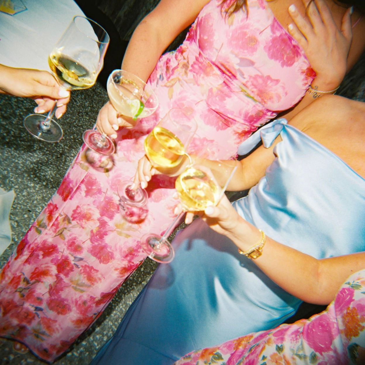 Friends toasting with cocktails wearing colorful floral dresses.