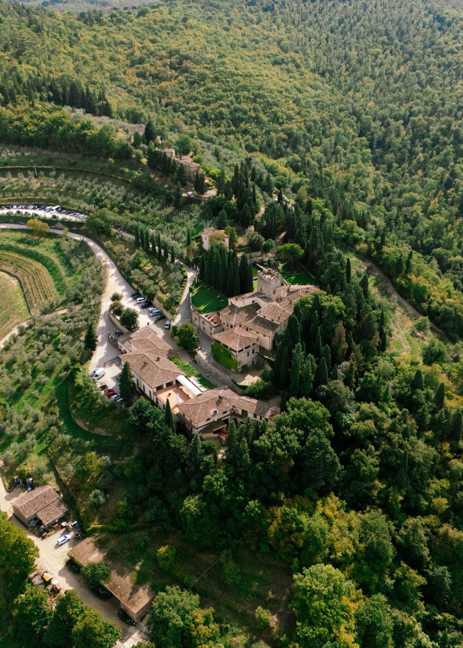 Aerial view of Tuscan villa nestled in rolling green hills with terraced gardens.