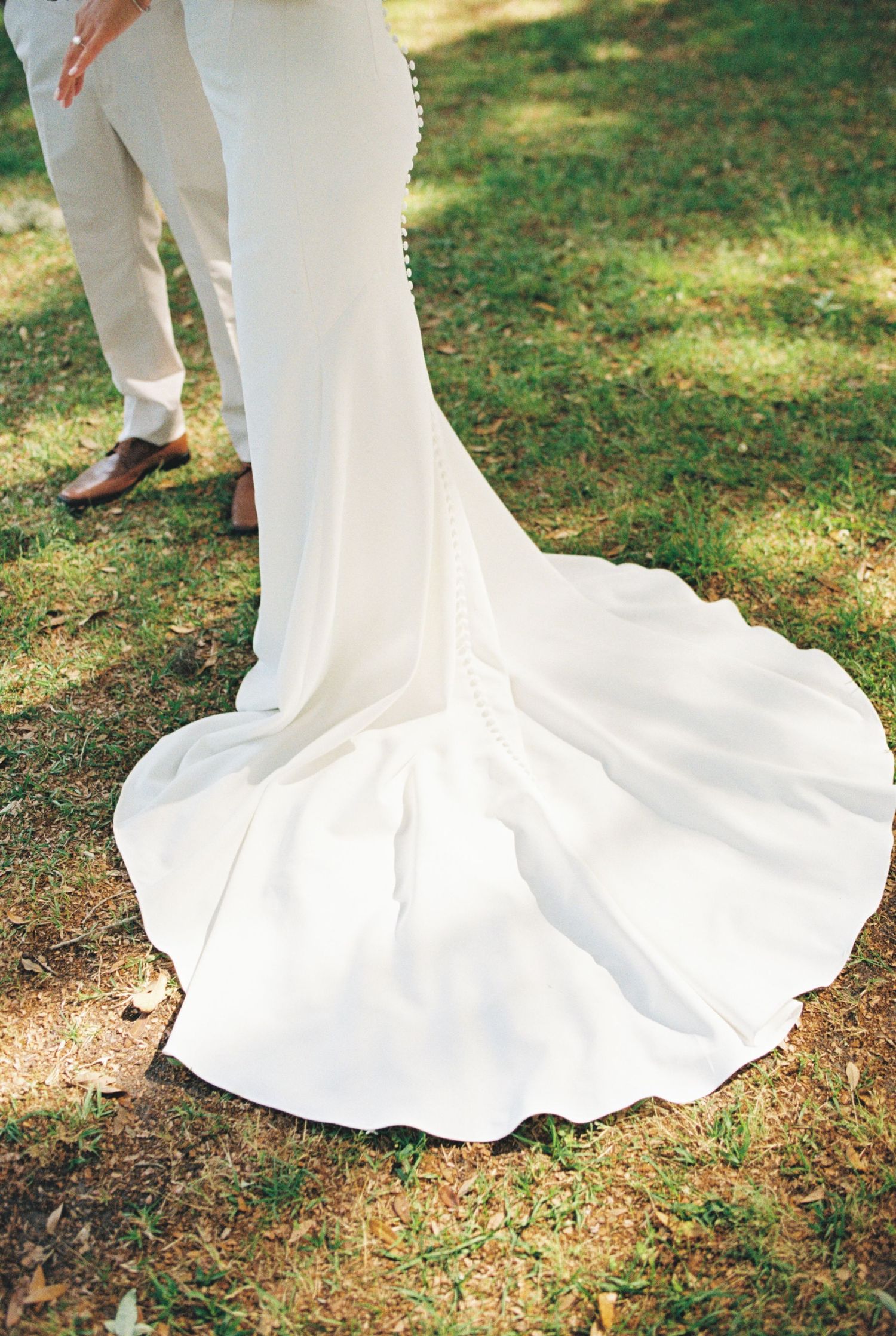 Elegant white wedding dress train flowing over grass in an outdoor setting.