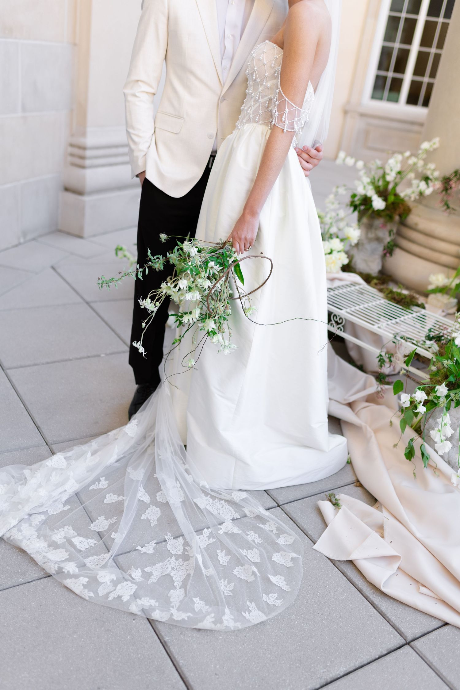 Close-up of an elegant white wedding dress train with lace details on stone patio.