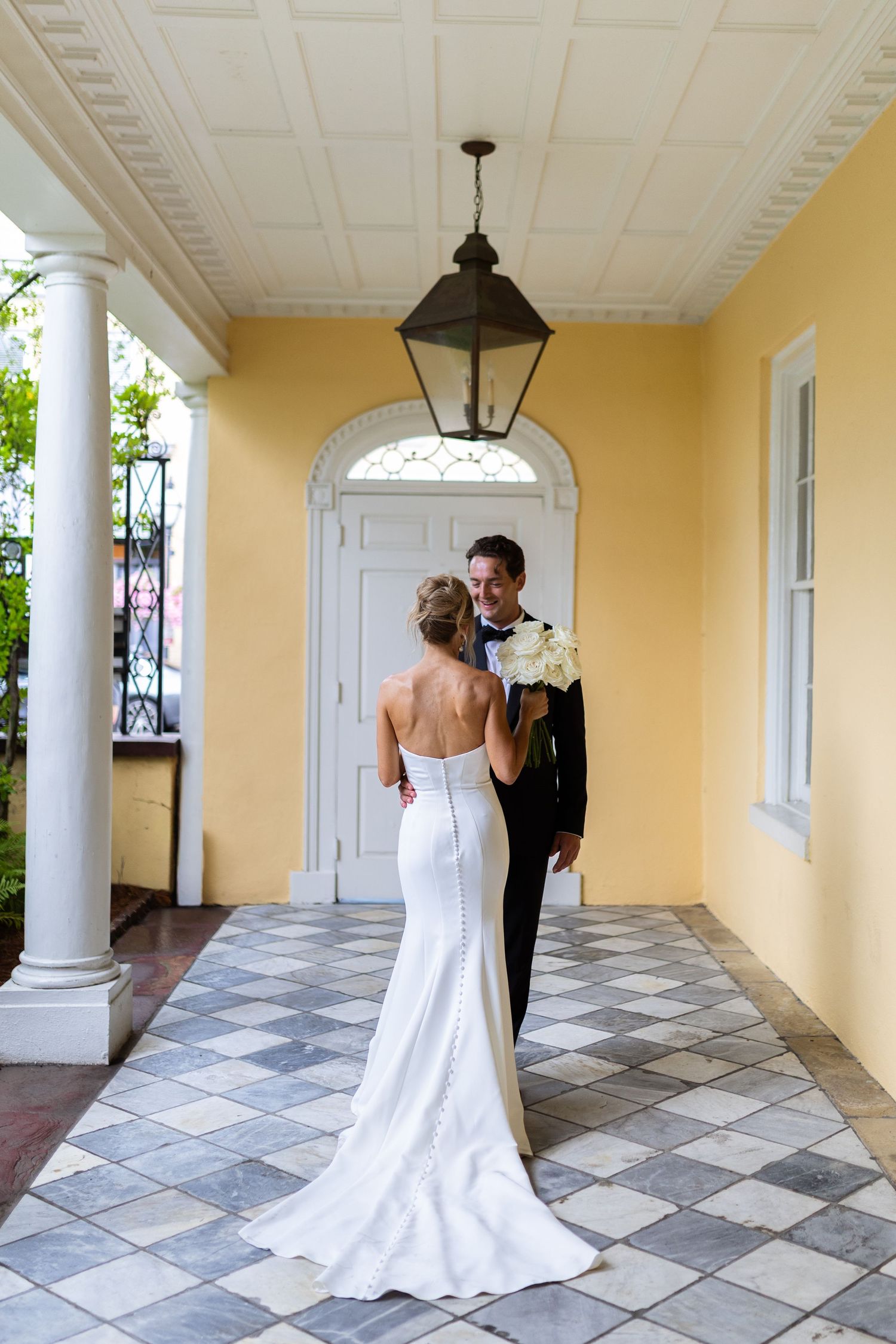 Elegant couple embracing on a yellow-walled porch with checkerboard tile floor.