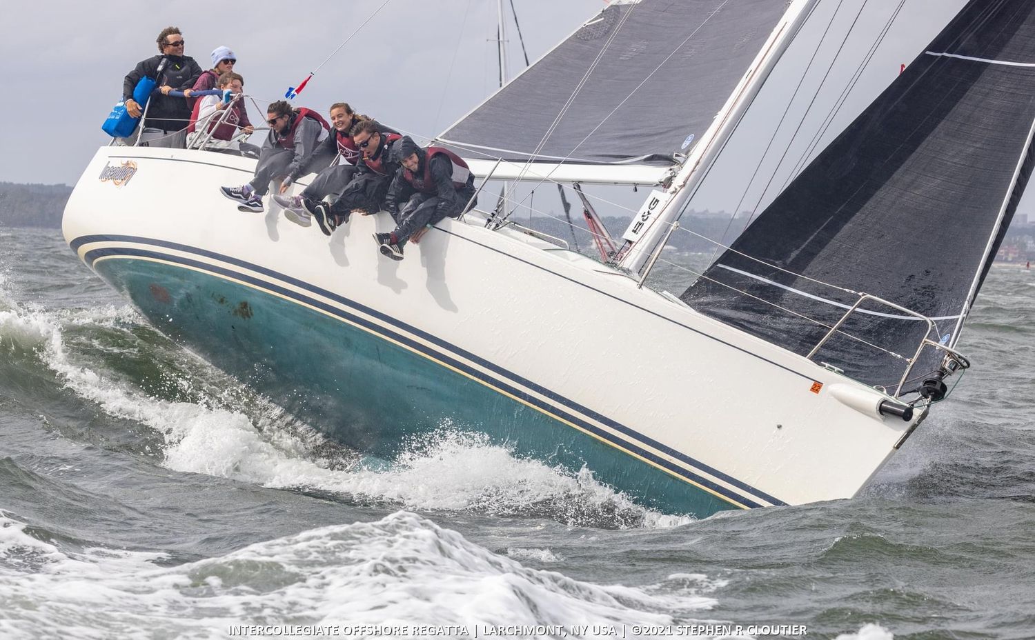 Sailboat heeling dramatically in rough waters during intense racing conditions.