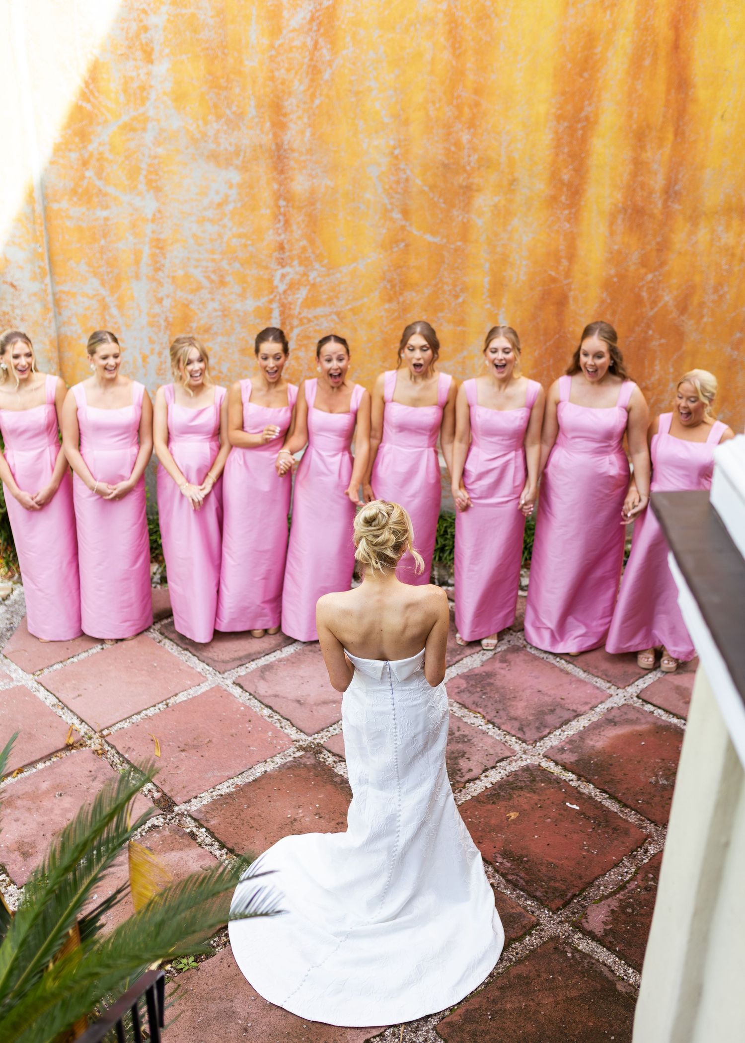 Bridesmaids in matching pink dresses pose together on rustic steps at a wedding.