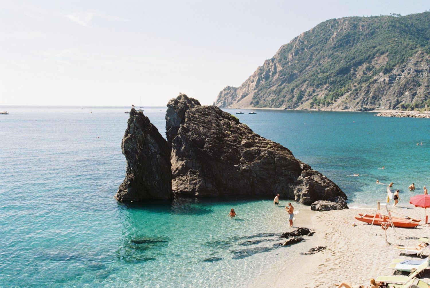 Rocky beach cove with large stone formation in crystal blue Mediterranean waters.