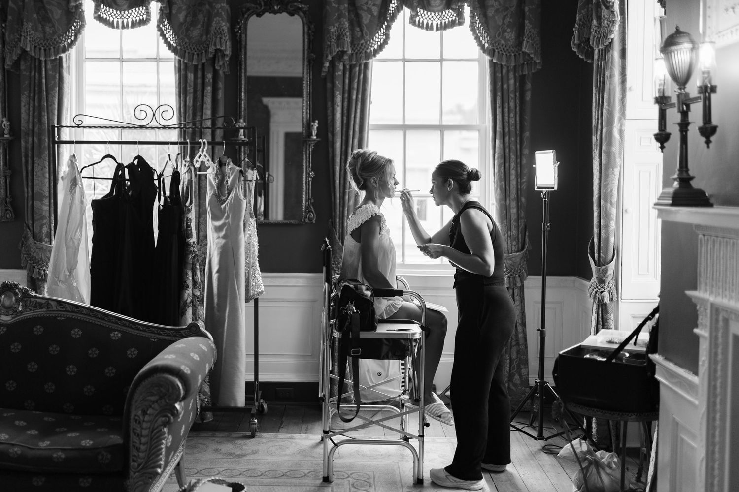 Black and white image of wedding preparation in an elegant room with tall windows.
