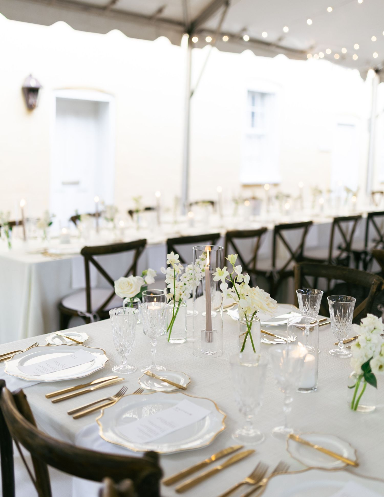An elegant wedding reception table setting with white linens and cross-back chairs.