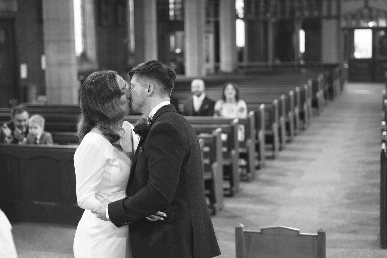 A romantic black and white moment captured in a church with wooden pews in the background.