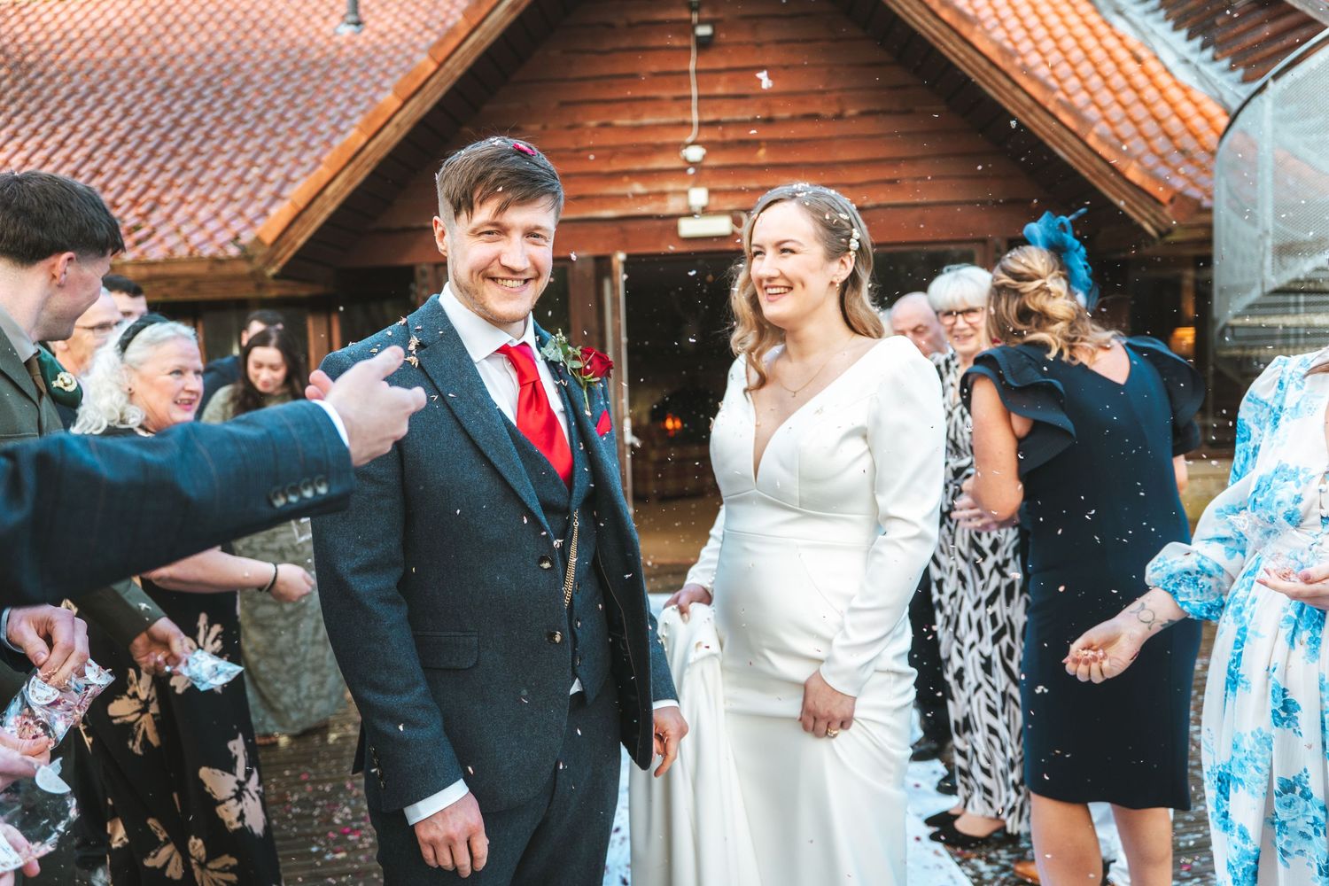 Wedding celebration with guests throwing confetti outside a wooden lodge.