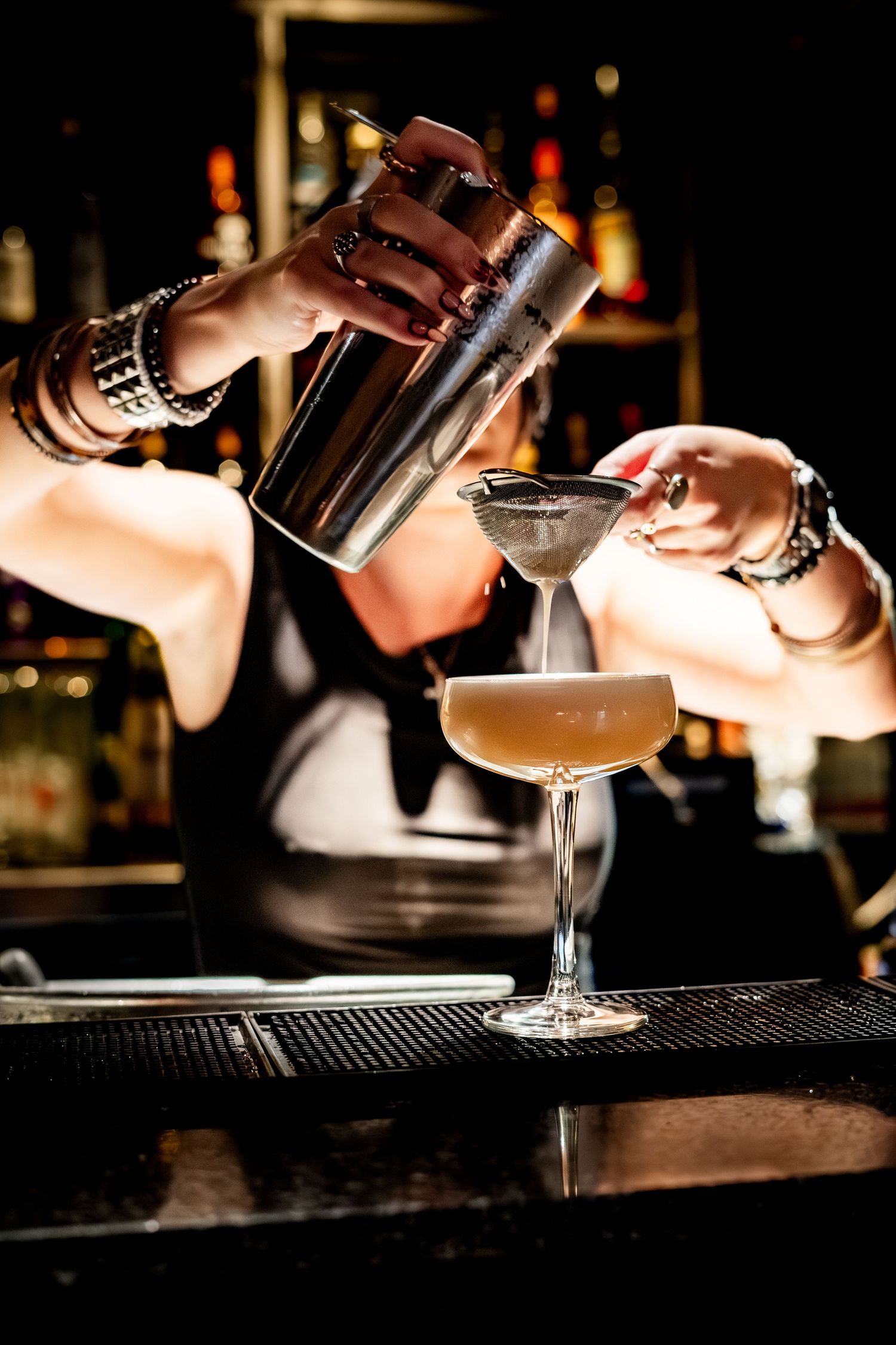 Hands pouring a shaken cocktail through a strainer into an elegant coupe glass.