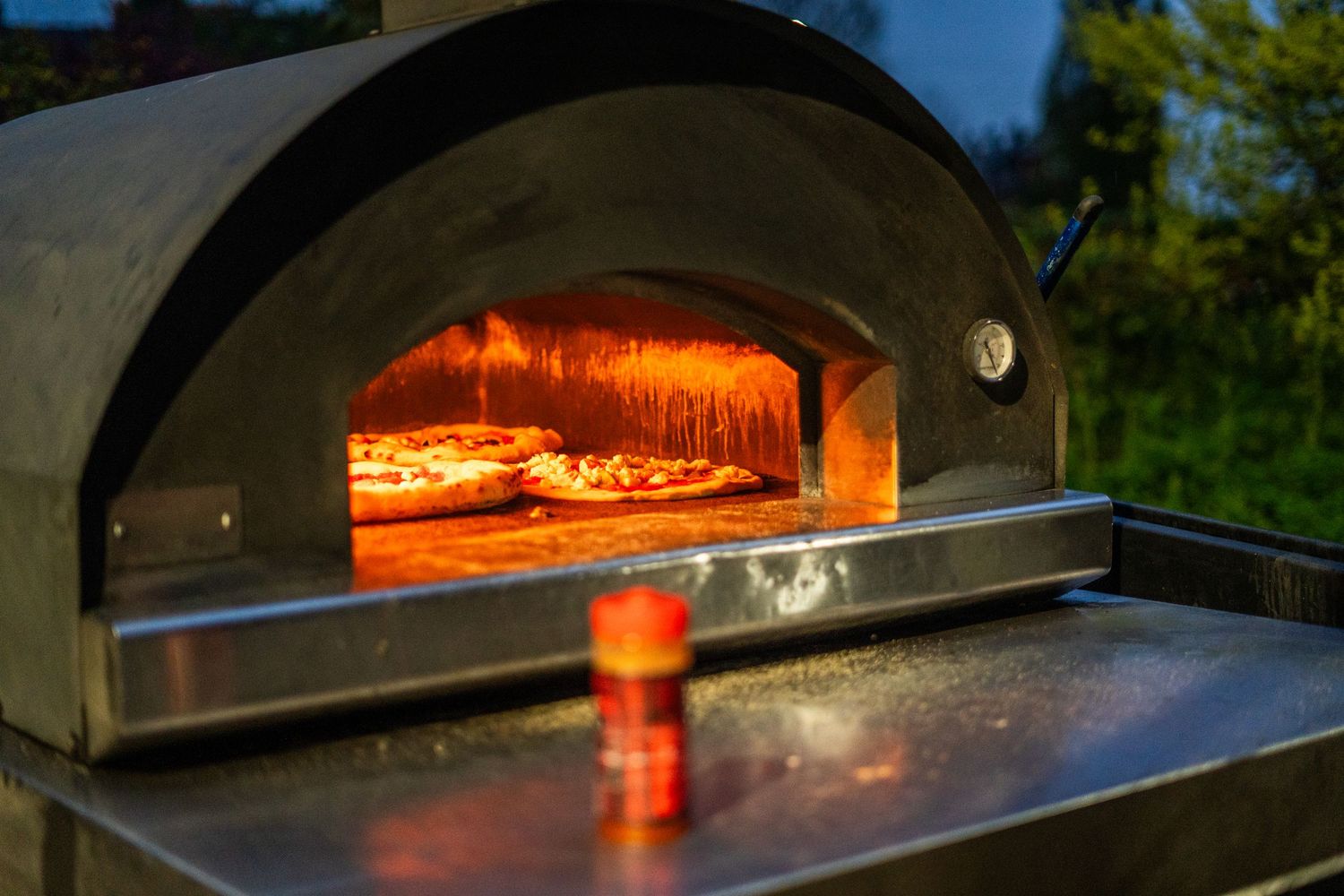 Wood-fired pizza oven with glowing flames visible through the opening.