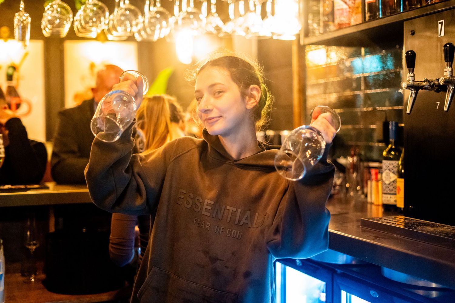Bar staff member examining wine glasses under ambient lighting.