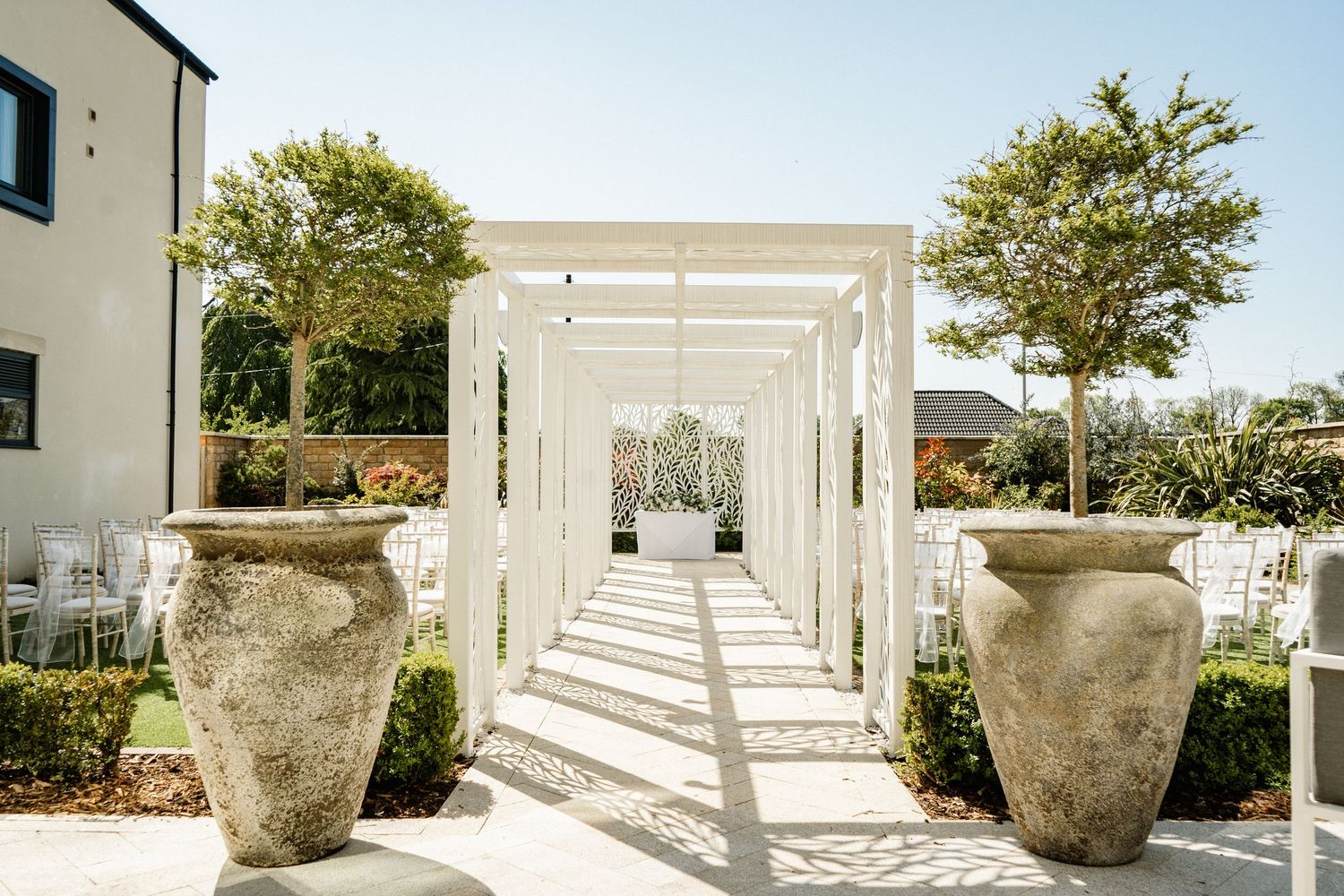 Modern white pergola and garden features with large decorative stone urns.