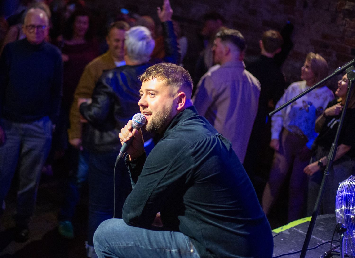 Live music performance in a dark venue with blue stage lighting and audience members visible.