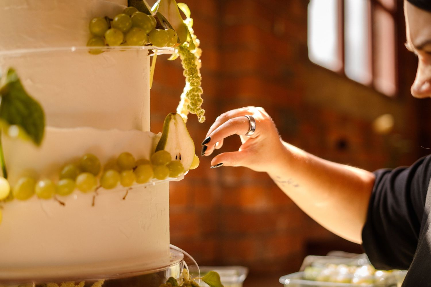 Wedding cake with fresh grape decorations in natural window light against brick wall.