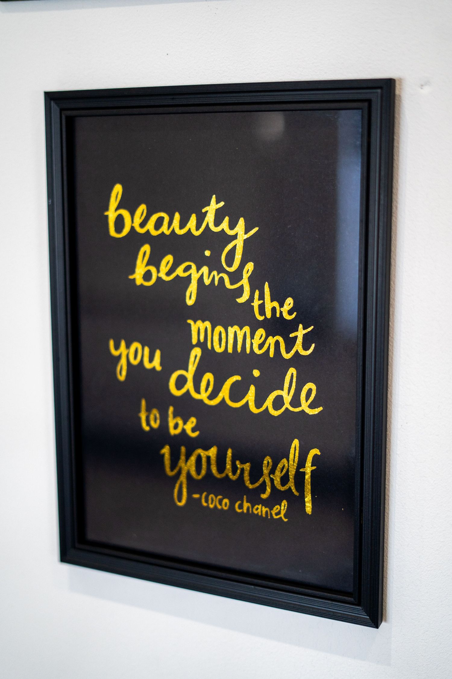 Black framed artwork with yellow cursive text about self-determination displayed on white wall.