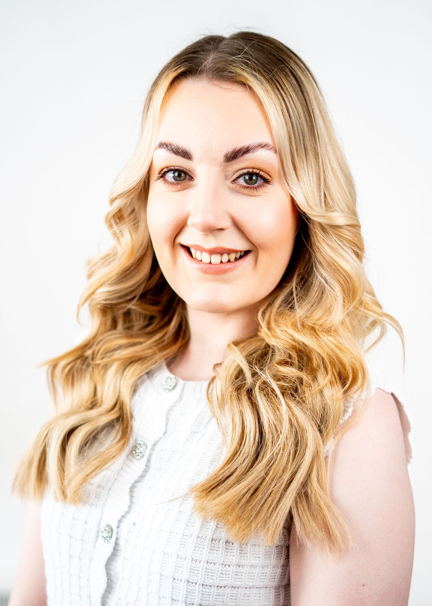 Professional headshot of a person with styled blonde waves wearing a white lace top.