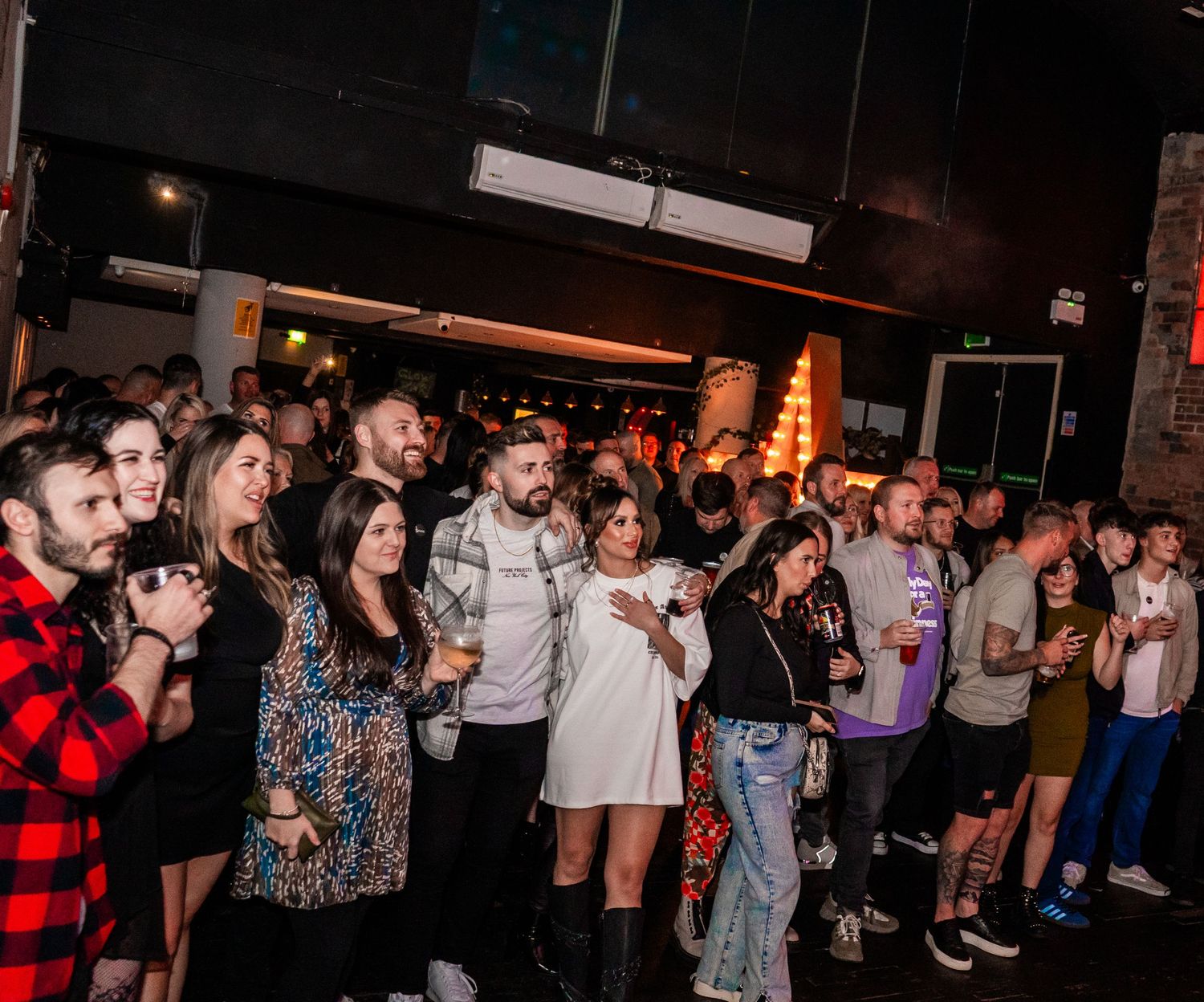 Wide shot of an enthusiastic audience at a music venue with warm ambient lighting.