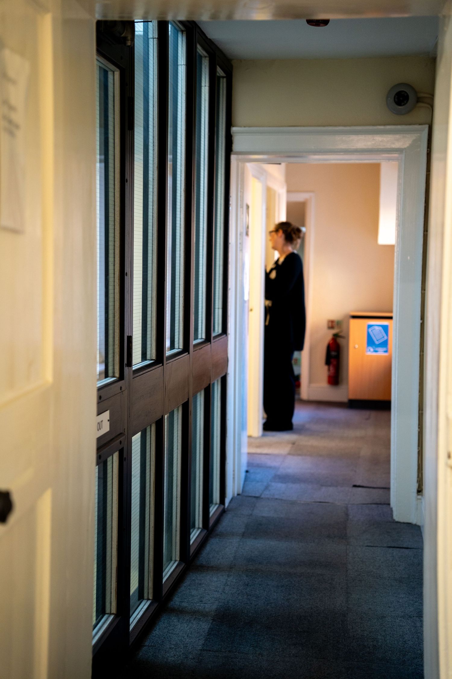 Long empty office hallway with glass windows and carpeted floors.