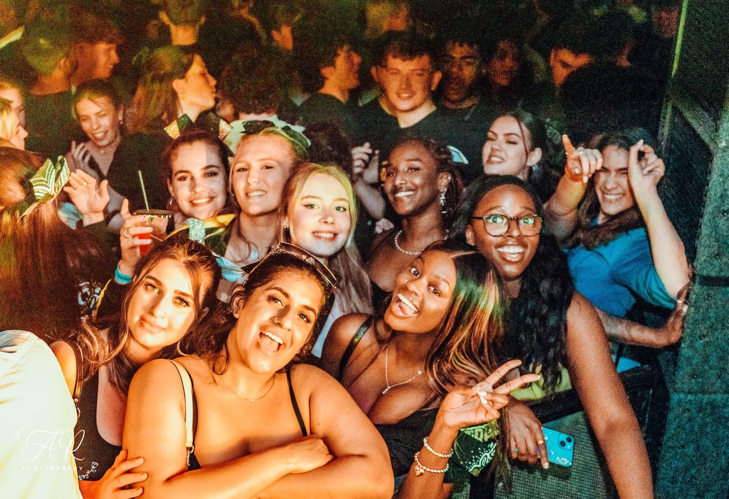 Excited crowd of partygoers enjoying a nightclub event with vibrant lighting and energetic atmosphere.