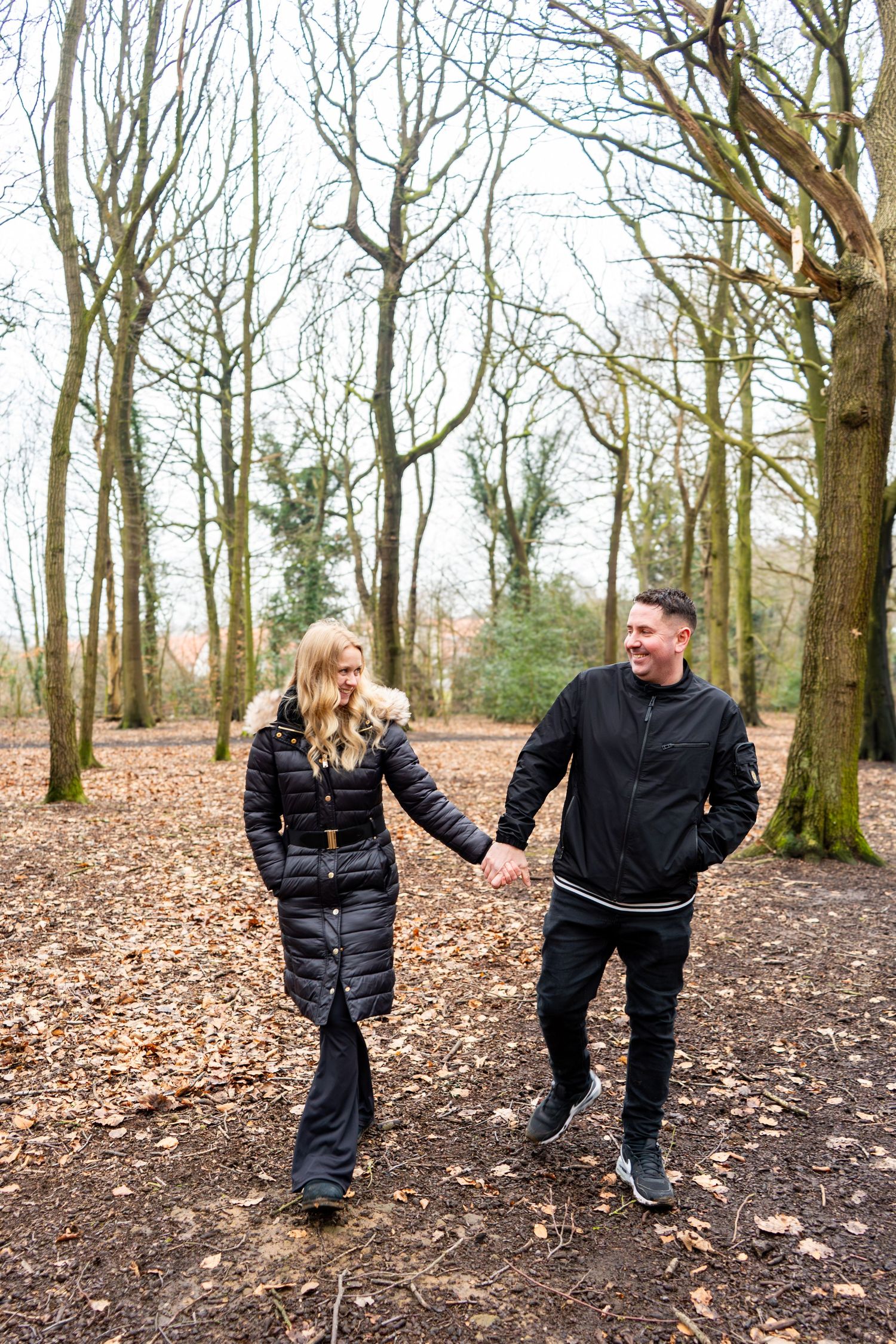 Couple dancing and laughing together on a leaf-covered forest path.
