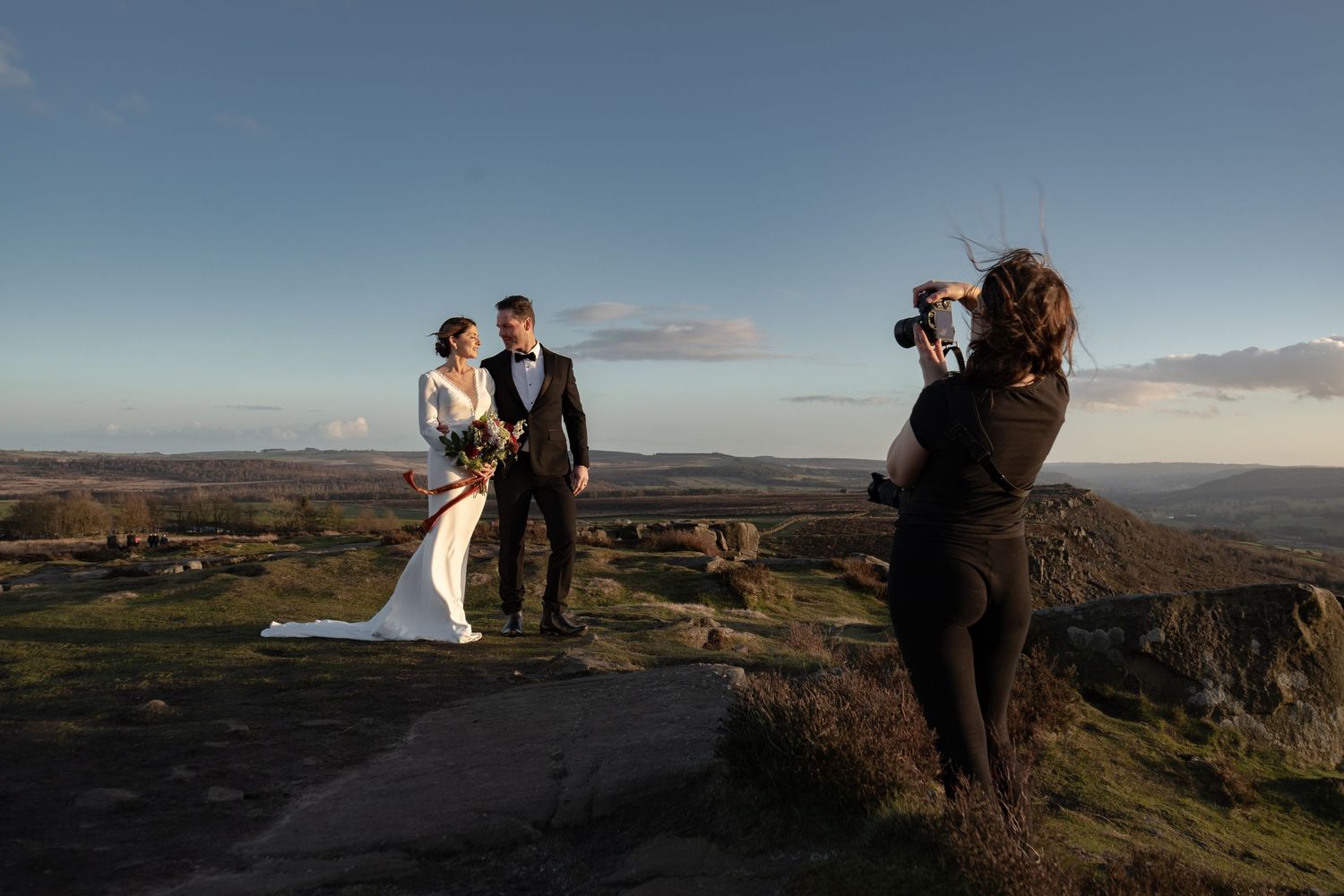 A wedding photography session taking place on a dramatic clifftop at sunset.
