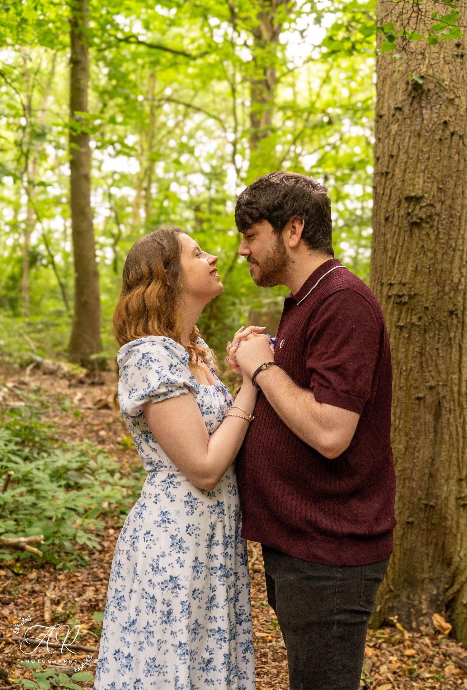 A couple shares a tender moment against a tree in a sunlit forest.