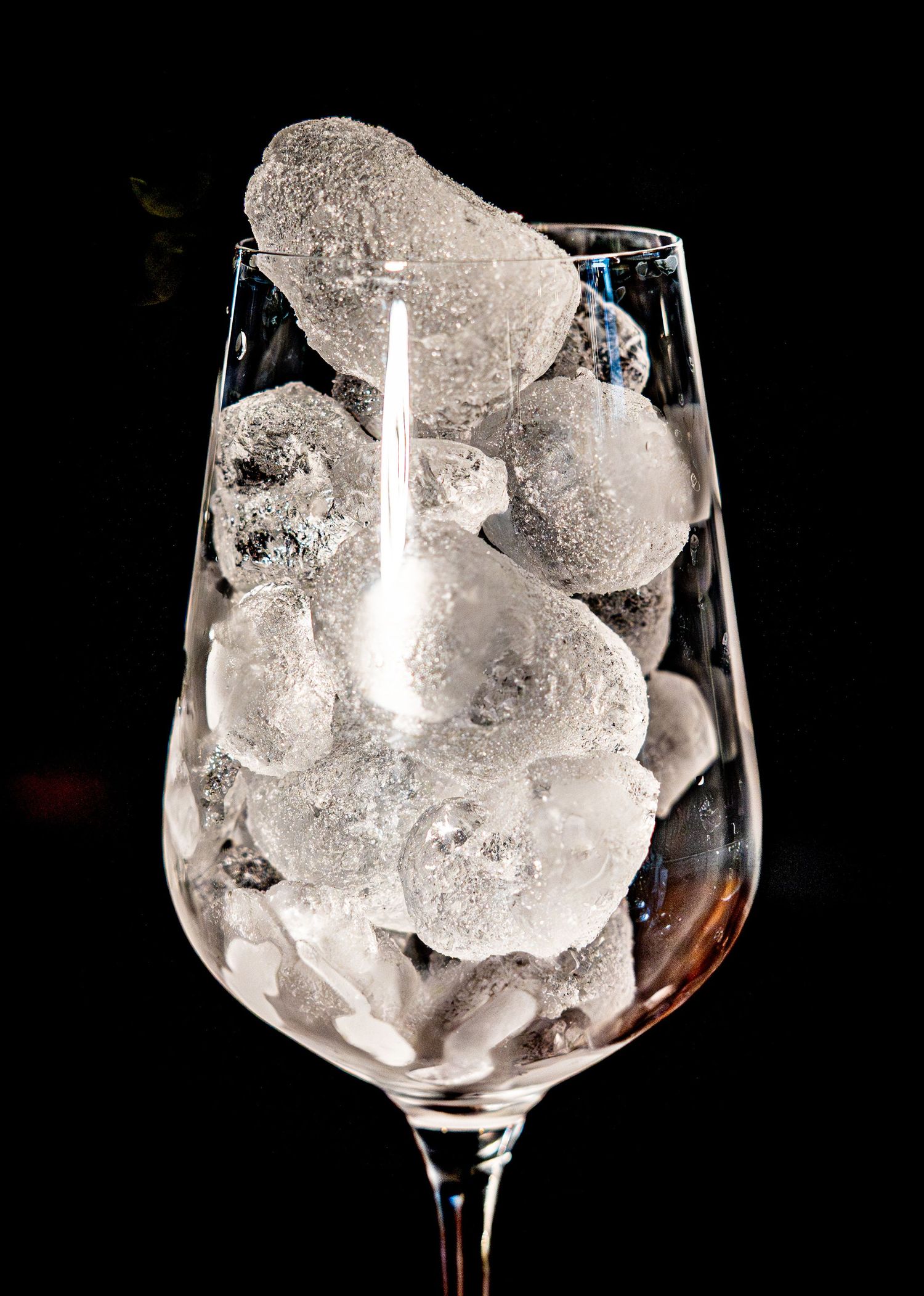 A wine glass filled with large clear ice cubes against a dark background.