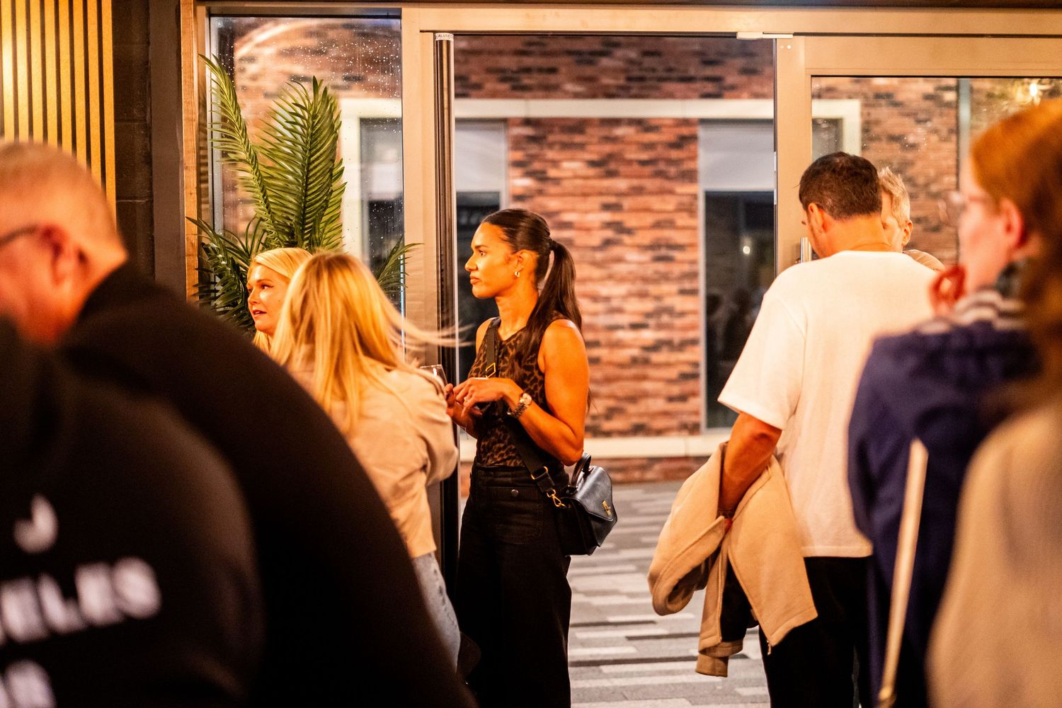 Crowd of people gathered outside venue entrance in evening light.