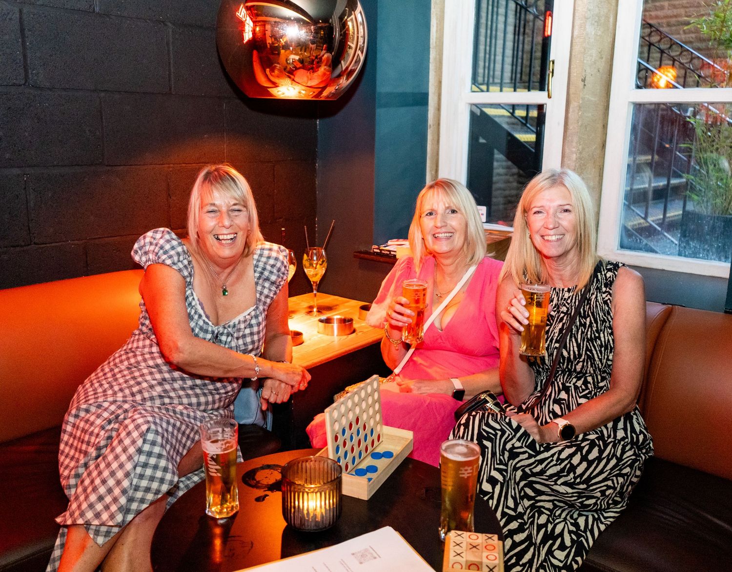 Friends gathered at a cozy bar lounge area with red ambient lighting.