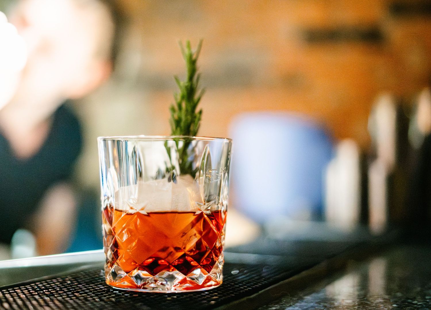 Red cocktails garnished with fresh herbs on a bar counter with warm ambient lighting.