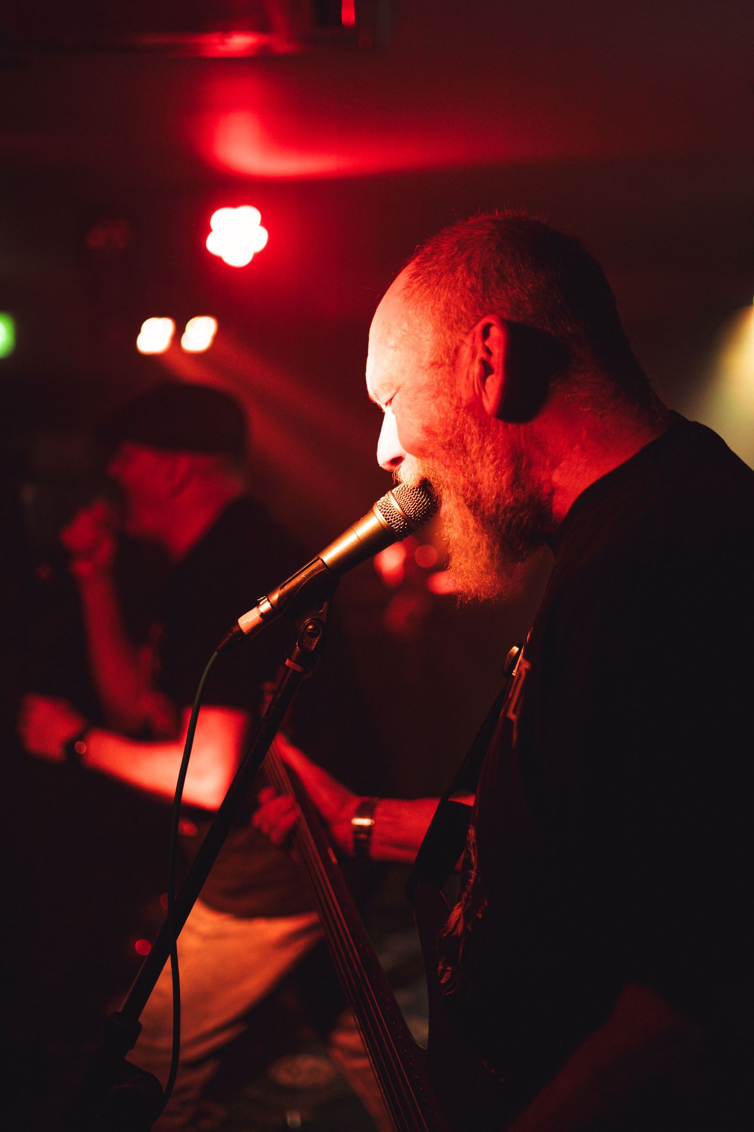 Musician performs on stage bathed in dramatic red lighting at a live concert venue.