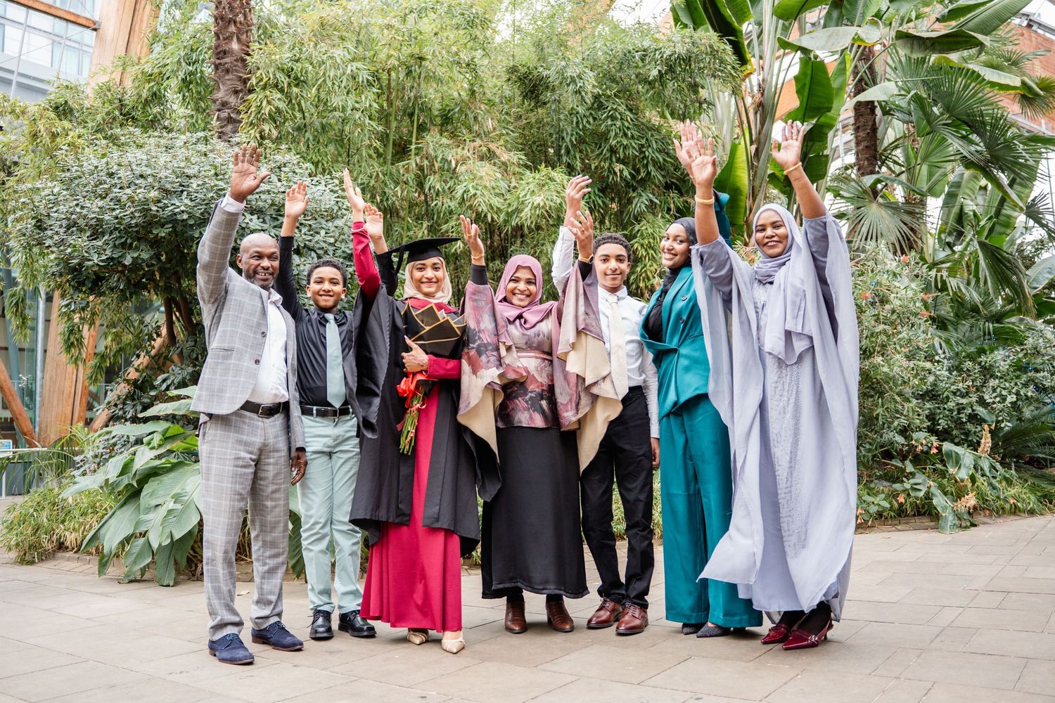 Group photo of wedding guests in colorful attire standing in a garden.