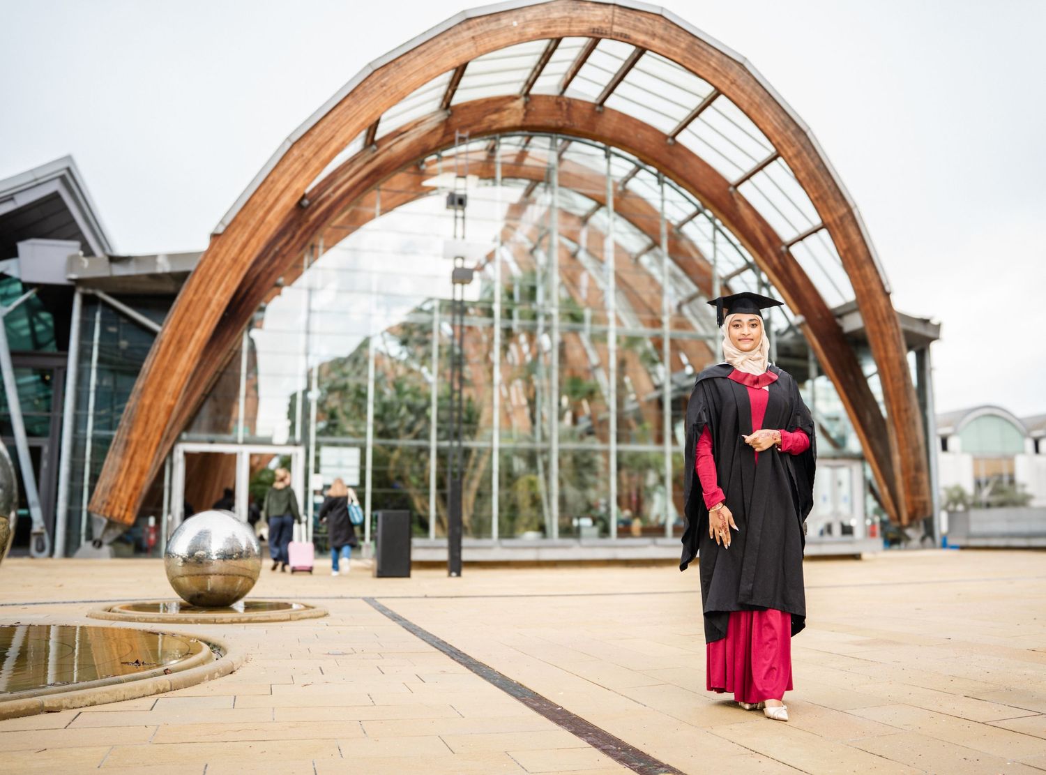 Architectural view of curved wooden beams with graduate posing beneath structure.