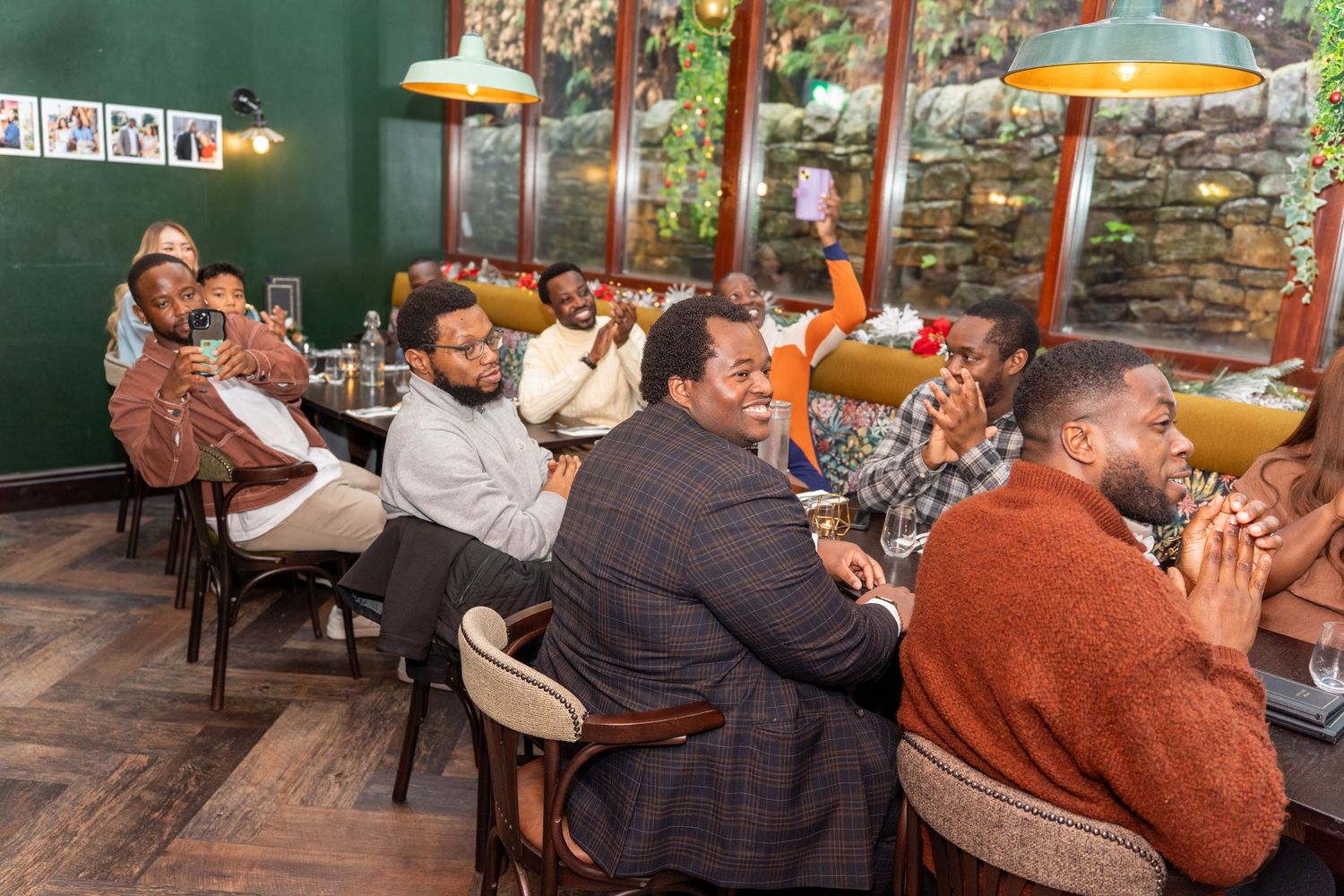 A group celebration with people seated at tables against a green wall background.