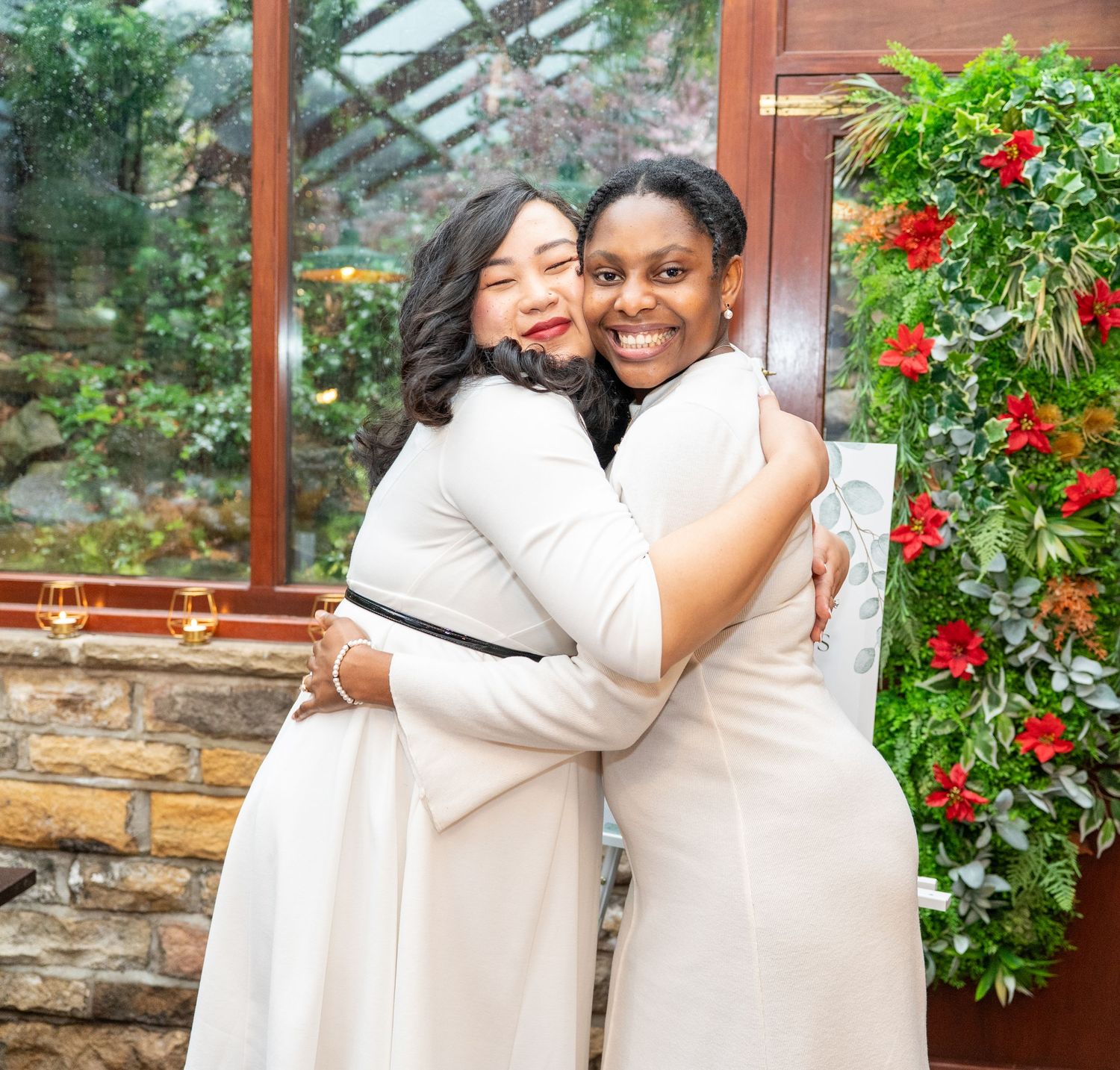Happy embraces shared between people wearing white outfits against a backdrop with red flowers.
