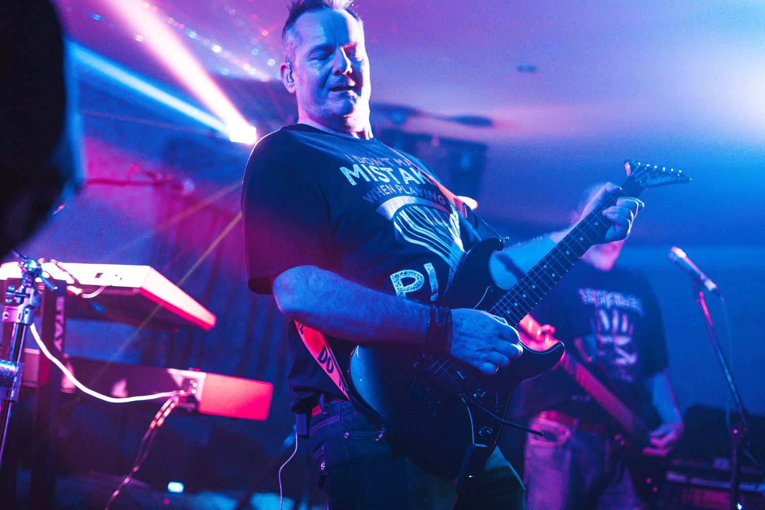 A guitarist performs on stage under dramatic blue lighting at a live music venue.