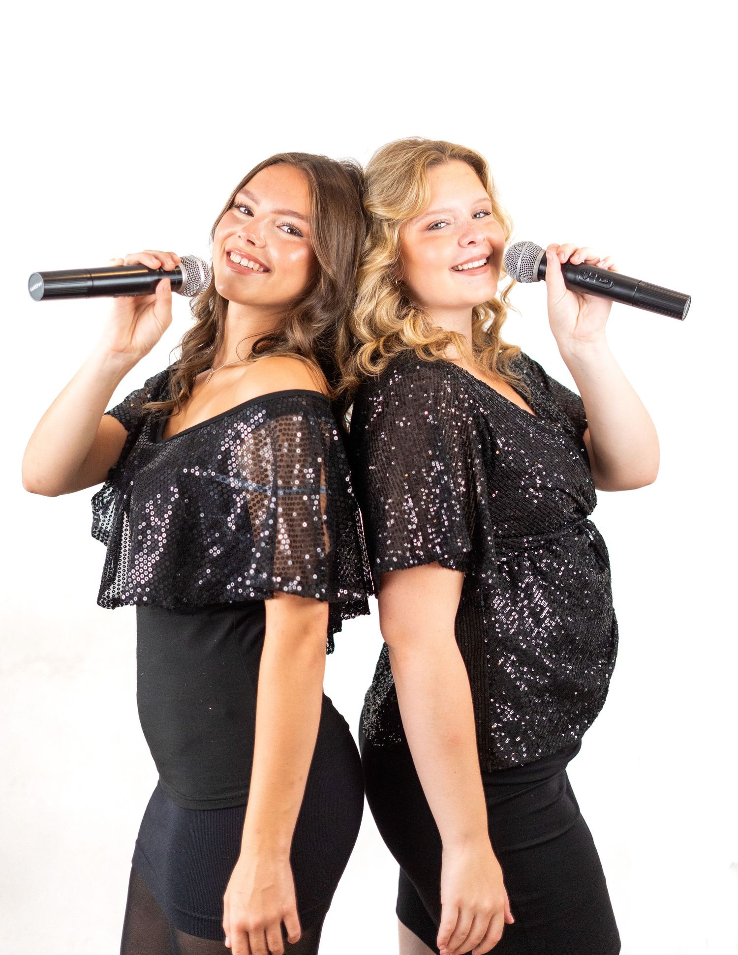 Two singers in coordinated black sparkly outfits perform together against white background.