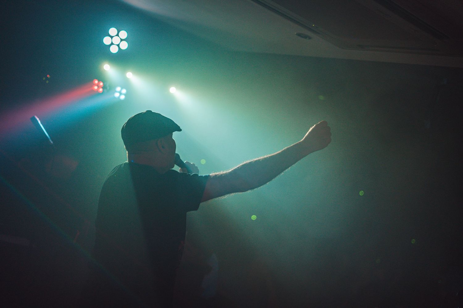 Silhouetted performer gesturing on stage with teal lighting effects.