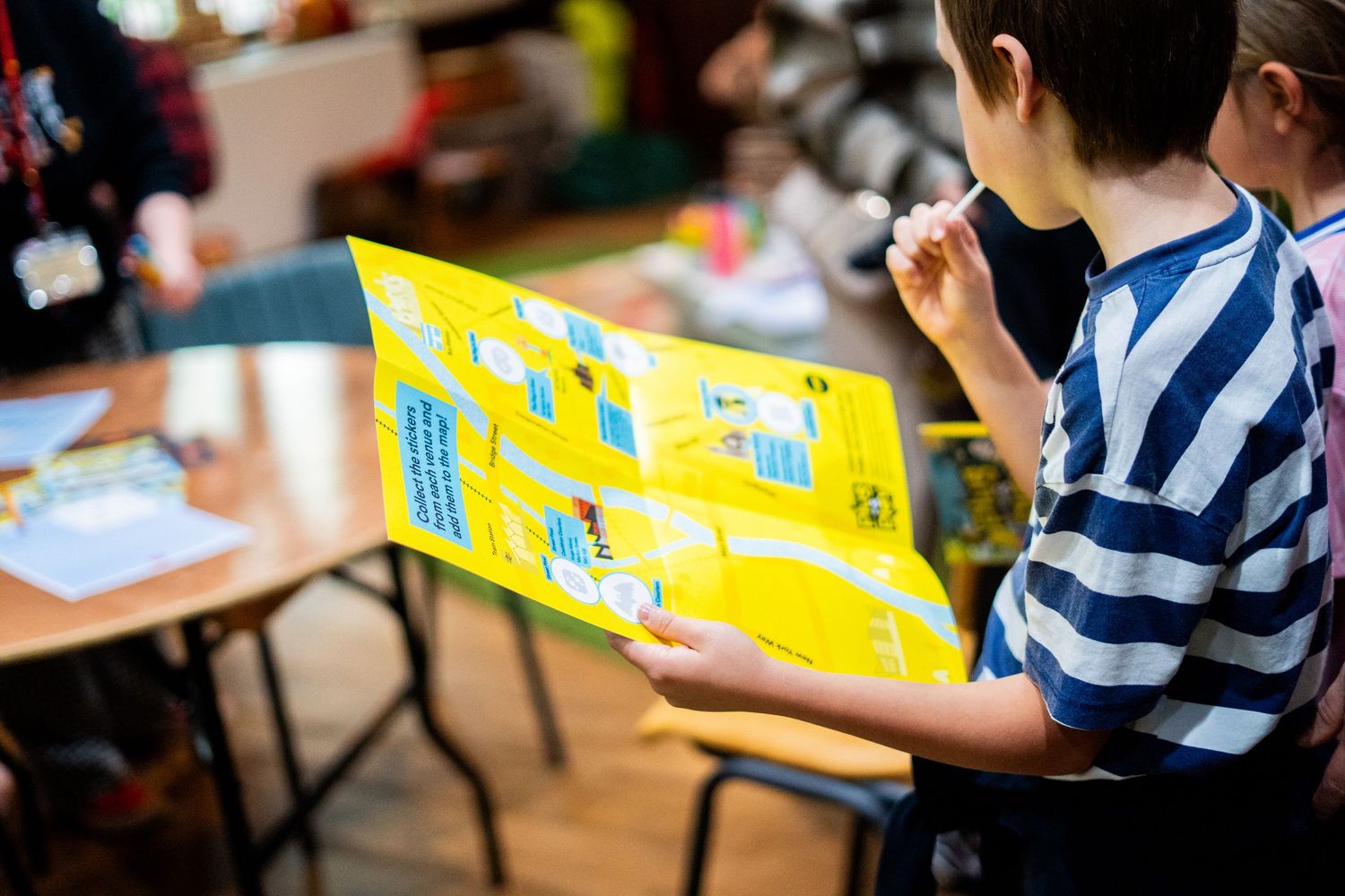 Child in striped shirt reading a yellow book while sitting at a desk.