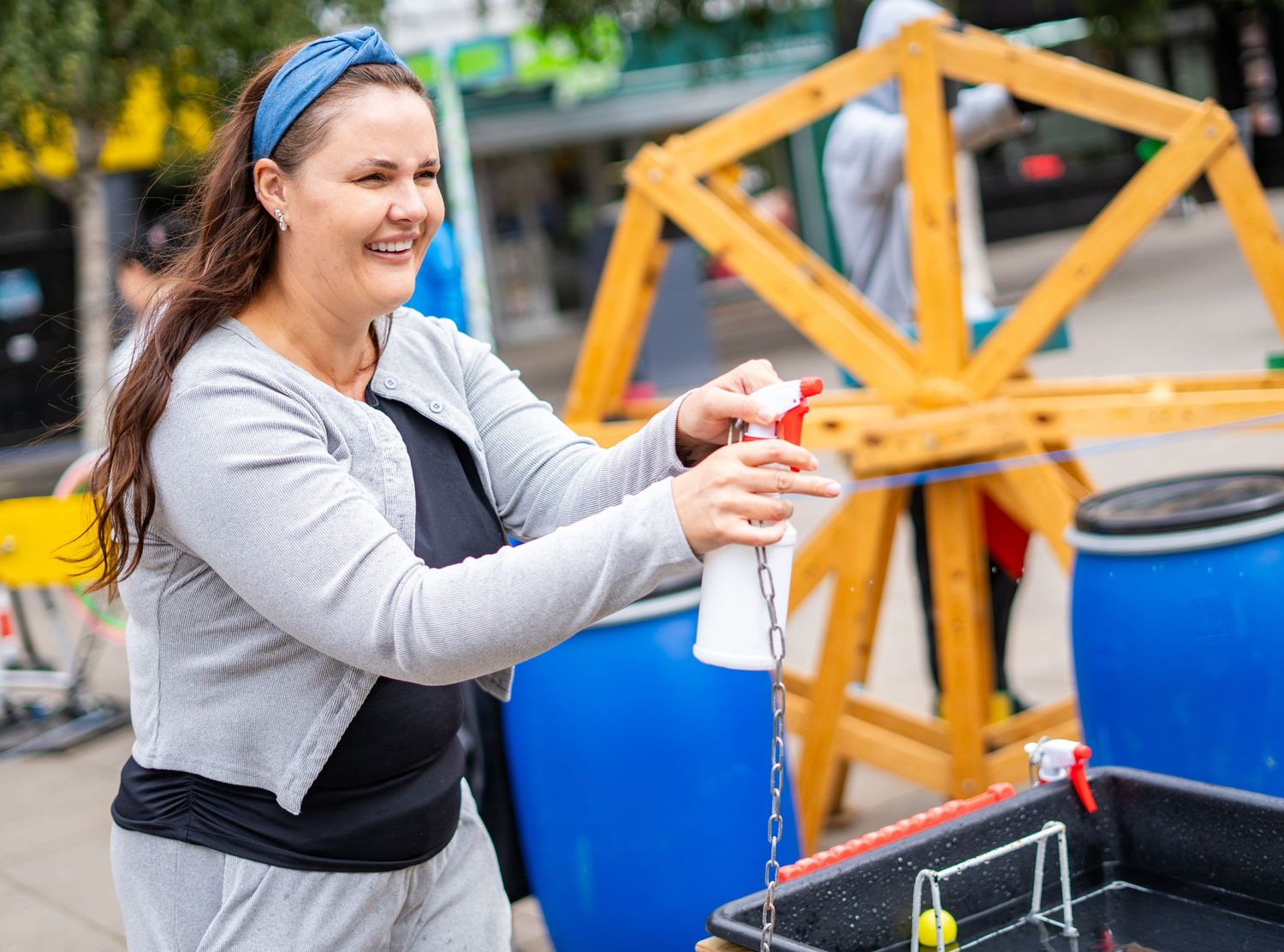 Woman in gray sweater playing with interactive display at outdoor event.