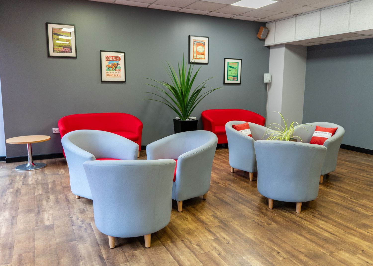 Modern office lounge area with gray walls, light blue chairs, and wooden flooring.