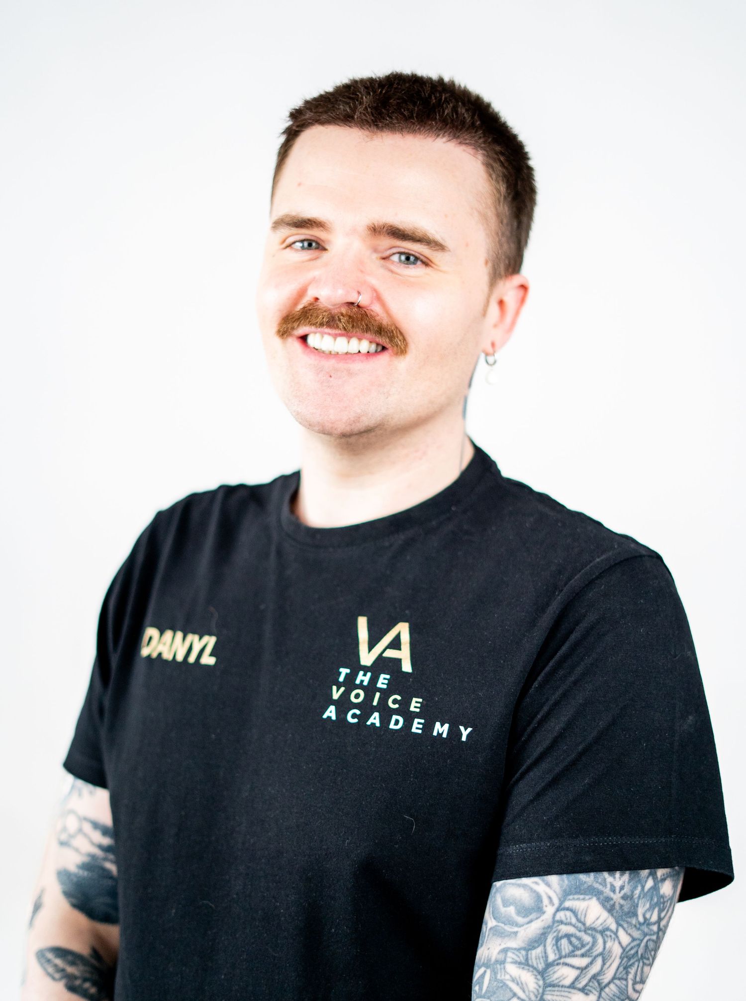 Professional headshot of a person with a mustache and tattoos wearing a black branded t-shirt.